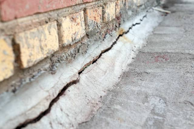 Quality Foundation Repair Austin inspecting a deep foundation crack at the base of a brick wall.
