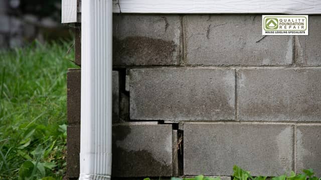 Quality Foundation Repair Austin inspecting stair-step cracks in a concrete block foundation with water damage near a downspo
