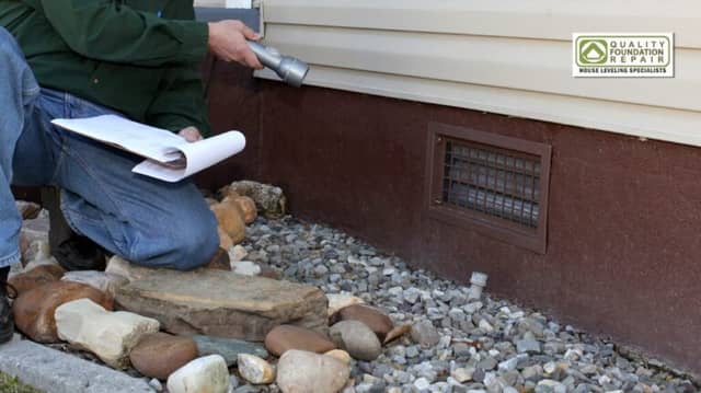 Quality Foundation Repair Austin technician inspecting a crawl space foundation vent with a flashlight and clipboard.