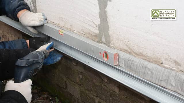 Quality Foundation Repair Austin technicians performing structural leveling and foundation repair using a level and drill.