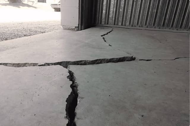 Quality Foundation Repair Austin inspecting severe cracks and unevenness in a concrete garage floor, typical signs of foundat