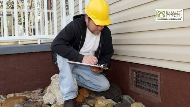 Quality Foundation Repair Austin technician performing a home foundation inspection near a crawl space vent, documenting find