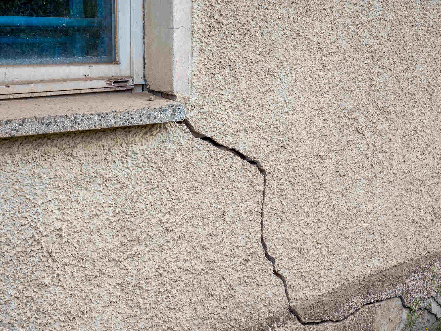 Quality Foundation Repair Austin inspecting a diagonal crack in a stucco exterior wall, indicating potential foundation movem