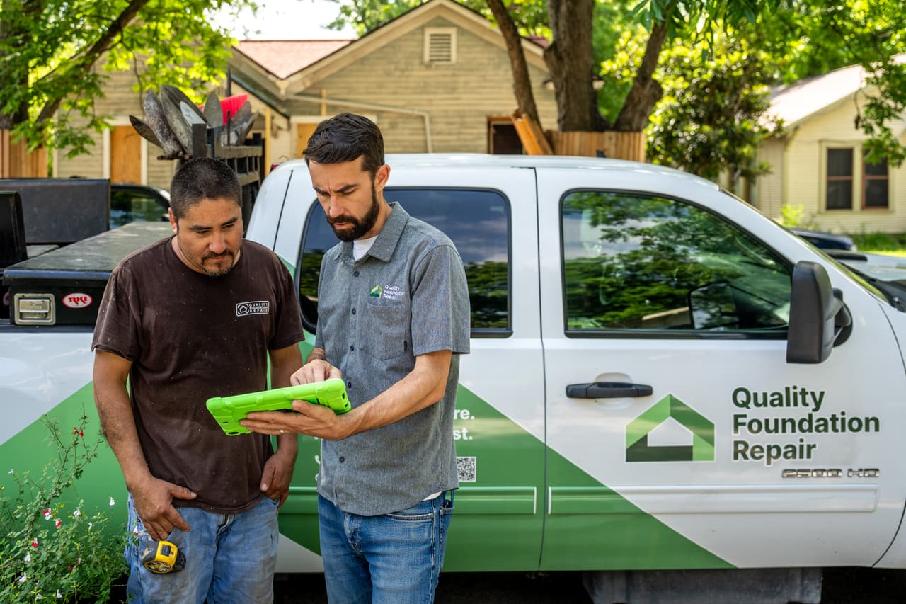 Quality Foundation Repair Austin team members reviewing a foundation inspection report on a tablet beside a branded truck.