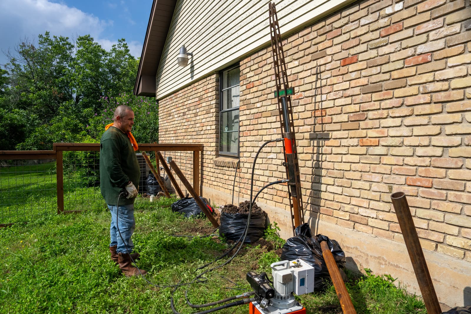 A Quality Foundation Repair Austin crew member installing steel push piers along the brick wall of a Central Texas home.