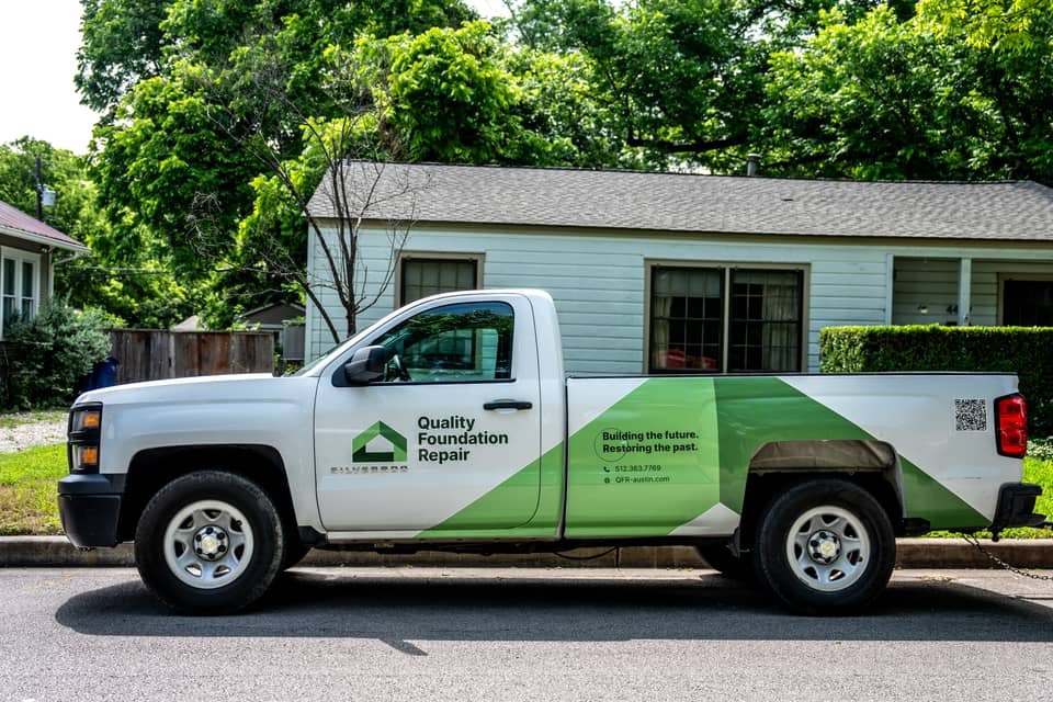 A Quality Foundation Repair Austin truck parked outside a home on a tree lined Central Texas street.